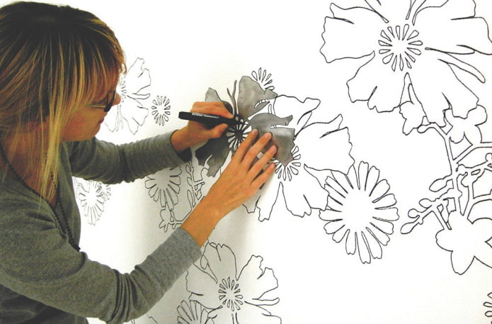 женщина рисует цветы на стене по трафарету